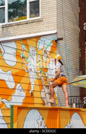 Un artiste sur une échelle peint une murale colorée avec des visages et des figures abstraites sur un mur du marché de Kensington. Banque D'Images