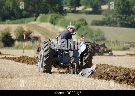 Agriculteur utilisant un tracteur d'époque dans les champs pendant le labourage. Labourage Vintage, Rousham, Angleterre Banque D'Images