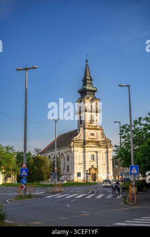 HODMEZOVASARHELY, HONGRIE 06 MAI 2022 Une grande église de couleur claire se dresse bien en évidence au centre d'une large intersection, sous un ciel bleu clair. Banque D'Images