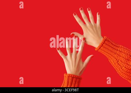 Femmes mains avec manucure rouge en pull orange. Concept de salon de beauté Banque D'Images