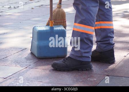 Le nettoyeur balaye le trottoir dans la zone du parc de la ville Banque D'Images