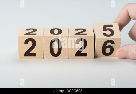 L'homme change d'année de 2025 à 2026 avec des blocs de bois. Symbolise la veille du nouvel an, la fin d'une période et le début d'une autre Banque D'Images