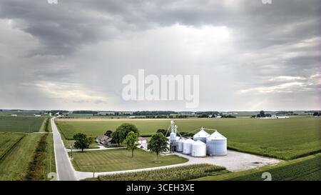 Vue aérienne d'un paysage rural où une route traverse des champs agricoles verdoyants menant à des bâtiments agricoles sous un ciel nuageux, Monroeville, I Banque D'Images
