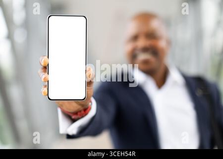 Homme d'affaires afro-américain tenant smartphone avec écran blanc vierge à l'aéroport Banque D'Images