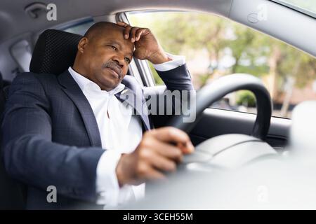 Homme d'affaires afro-américain stressé conduisant une voiture ayant l'air fatigué ou ennuyé Banque D'Images