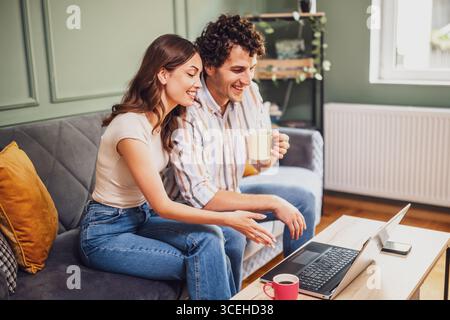 Un couple adulte passe un appel vidéo avec sa famille. Homme et femme assis au canapé à la maison et à l'aide d'un ordinateur portable. Banque D'Images