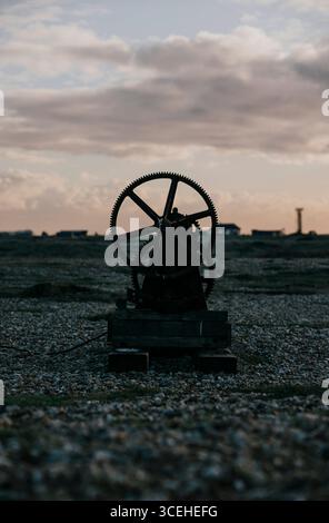 Une vieille roue rouillée est assise sur un champ rocheux. Le ciel est nuageux et le soleil se couche Banque D'Images