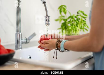 Les mains d'une femme lavant Une tomate à la maison dans la cuisine Banque D'Images
