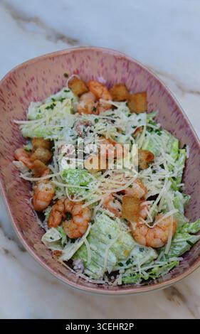 Salade César fraîche servie dans un bol en céramique rose avec crevettes grillées, laitue romaine croquante, parmesan, croûtons croustillants et vinaigrette crémeuse. Banque D'Images