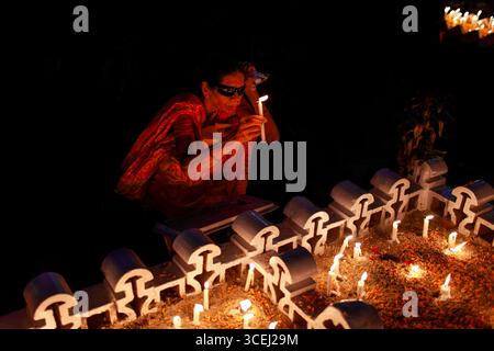 Chattogram, Bangladesh - 02 novembre 2022 : vue d'une femme dans un sari rouge vif agenouillée pour allumer une bougie au milieu de rangées de petites structures blanches, projetant une lueur chaude et douce contre la nuit profonde. Banque D'Images