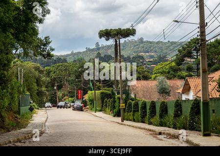 Scène de rue de Mantiqueira, avec des voitures garées, des maisons traditionnelles et des montagnes verdoyantes sous un ciel nuageux dense après-midi d'été. Banque D'Images