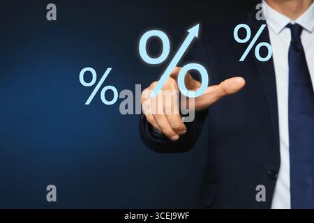 Homme d'affaires touchant le signe de pourcentage virtuel sur fond bleu foncé, gros plan Banque D'Images