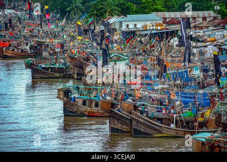 Patuakhali, Bangladesh - 05 septembre 2019 : vue d'un rassemblement dense de bateaux de pêche, leurs coques en bois reflétant la lumière de la rivière sous un ciel couvert. Banque D'Images