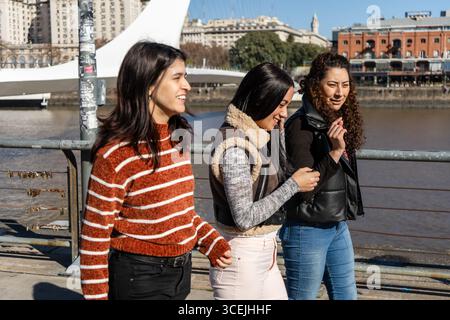 Trois jeunes femmes profitent d’une journée ensoleillée, discutant et riant ensemble au bord de la rivière dans le quartier de puerto madero à buenos aires Banque D'Images