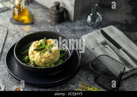 Risotto crémeux aux asperges et fromage râpé servi sur une assiette noire, prêt à être dégusté Banque D'Images