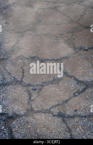 Chaussée asphaltée brisée, fissures humides forme la surface. Banque D'Images