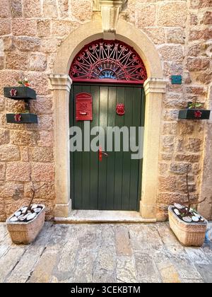 Une porte en bois vert avec boîte aux lettres rouge et cadre en pierre arquée sur un mur rustique. Architecture, tradition, entrée et identité résidentielle en urbain Banque D'Images