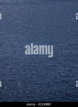 gros plan de l'eau sur un lac avec le soleil scintillant sur l'eau bleue créant des étincelles de blanc brillant sur la surface lors d'une belle journée d'été Banque D'Images