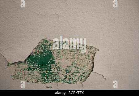 plâtre peint pelé du mur extérieur en béton de ciment révélant une couche de taches vertes sous un motif de taches et une forme étrange abstraite horizontale Banque D'Images