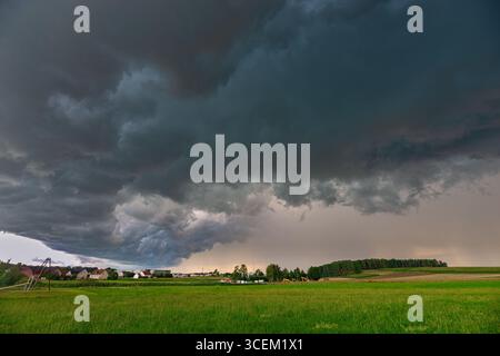 Le ciel sombre contraste fortement avec un champ vert vif tandis que le bord d'un orage se déplace au-dessus de la campagne en Bavière, en Allemagne Banque D'Images
