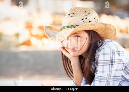 Jolie fille portant un chapeau de cowboy appréciant le Patch de citrouille sur un jour d'automne ensoleillé. Banque D'Images