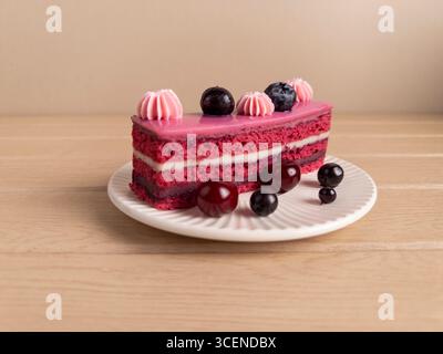 Photo rapprochée d'un gâteau éclatant à l'arôme des baies avec glaçage rose, décoré de crème fouettée, de cerises et de myrtilles. Servi sur un pl blanc Banque D'Images