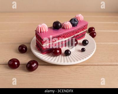 Une tranche de gâteau superposé magnifiquement présentée avec un glaçage rose, décorée de bleuets et de poupées crème rose, placée sur une assiette blanche. Le gâteau Banque D'Images