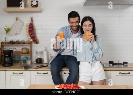 Jeune couple appréciant le jus d'orange frais dans la cuisine moderne, style de vie décontracté, amour et relation, matin joyeux ensemble, boisson saine, positiv Banque D'Images