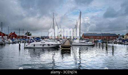 Port de plaisance côtier avec des bateaux amarrés le long du port, entouré de bâtiments pittoresques en bord de mer et une atmosphère calme sous un ciel ensoleillé. Banque D'Images