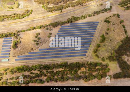 Vue aérienne d'une ferme solaire se prélassant sous le soleil, panneaux alignés en rangées soignées au milieu de champs secs et d'arbres dispersés, Breamlea, Victoria, Australie. Banque D'Images