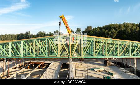 Vue de face rapprochée de fermes de toit en bois vert installées par une grue télescopique mobile sur un grand chantier de construction en béton et en brique avec for Banque D'Images