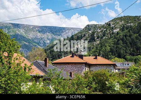 Vue panoramique sur les maisons traditionnelles des Balkans avec des toits rouges nichés parmi les arbres verdoyants et les montagnes majestueuses. Banque D'Images