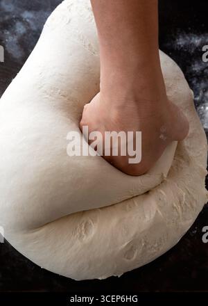 Gros plan des mains pétrissant la pâte dans la cuisine. Étape de préparation pour pain ou pizza avec pâte élastique levée. Banque D'Images