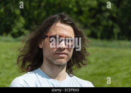 Portrait de lunettes brune homme se sentant mal, dépression, malheureux au parc et cadre naturel vert. Banque D'Images