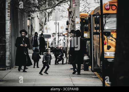 New York, États-Unis - 25 décembre 2023 : vue de membres de la communauté juive orthodoxe marchant près d'un autobus scolaire jaune vif, créant une étude en con Banque D'Images