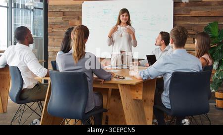 Femme d'affaires devant le tableau blanc présentation aux collègues autour de la table au bureau Banque D'Images