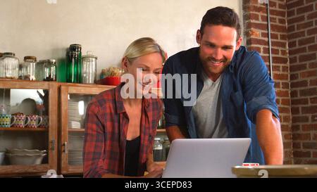 Jeune couple utilisant un ordinateur portable dans la cuisine ouverte de l'appartement Banque D'Images