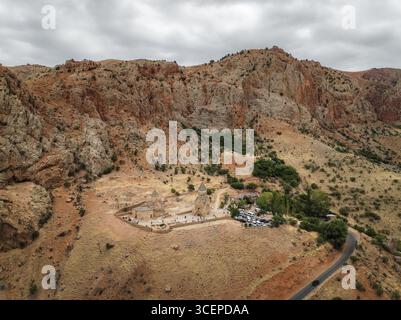 Vue aérienne du monastère de Noravank niché contre des falaises rouges escarpées sous un ciel nuageux, un témoignage de l'architecture ancienne, Vayots Dzor, Arménie. Banque D'Images