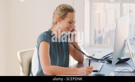 Jeune femme d'affaires travaillant au bureau sur ordinateur parlant au téléphone Banque D'Images