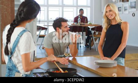 Couple parlant aux invités tout en préparant Food for Dinner Party à la maison dans la cuisine moderne Banque D'Images