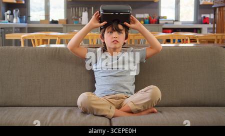 Garçon assis sur un canapé à la maison portant un casque de réalité virtuelle Banque D'Images