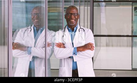 Portrait d'un médecin masculin senior souriant portant un manteau blanc debout dans le bâtiment de l'hôpital moderne Banque D'Images