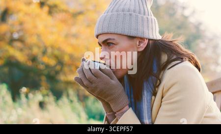 Femme assise sur le banc dans le parc d'automne ou la campagne avec boisson chaude Banque D'Images
