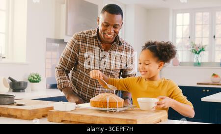 Photo de famille avec le père et la fille qui cuit à la maison dans la cuisine gâteau de décoration avec glaçage Banque D'Images