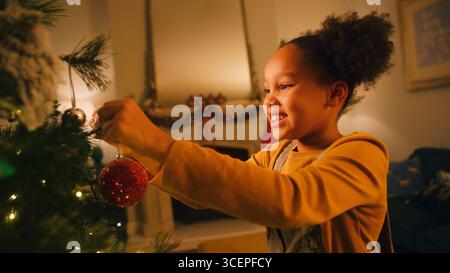 Excité fille à la maison accrochant décoration de Noël sur l'arbre Banque D'Images