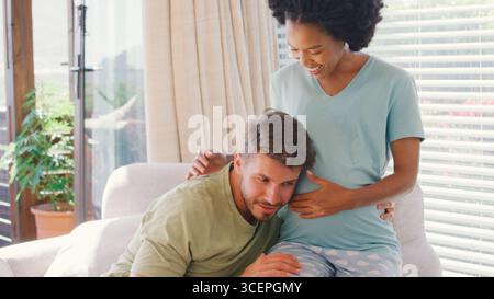 Couple multi-racial avec femme enceinte dans la chambre à coucher à la maison avec l'homme écoutant le battement de coeur de bébé Banque D'Images