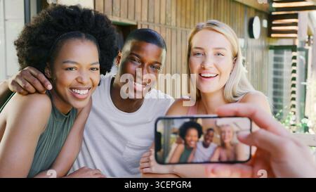 Amis multiculturels posant pour Selfie sur téléphone portable à l'extérieur à la maison Banque D'Images