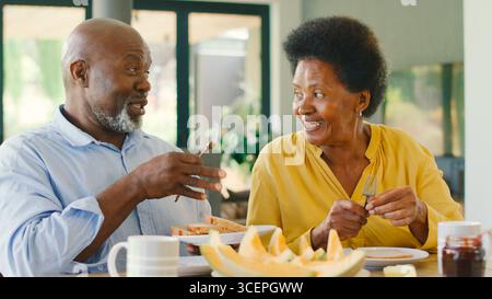 Couple senior à la maison profitant du petit déjeuner autour de la table ensemble Banque D'Images