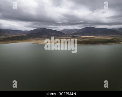 Vue aérienne du réservoir Spandarian tranquille sous un ciel sombre, les eaux sombres contrastant avec le paysage accidenté et montagneux, réservoir Spandarian, Syunik, Arménie. Banque D'Images