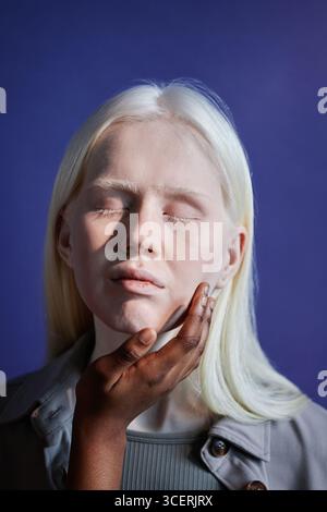 Gros plan vertical en studio d'une personne noire méconnaissable touchant doucement le visage d'une jeune femme caucasienne atteinte d'albinisme Banque D'Images